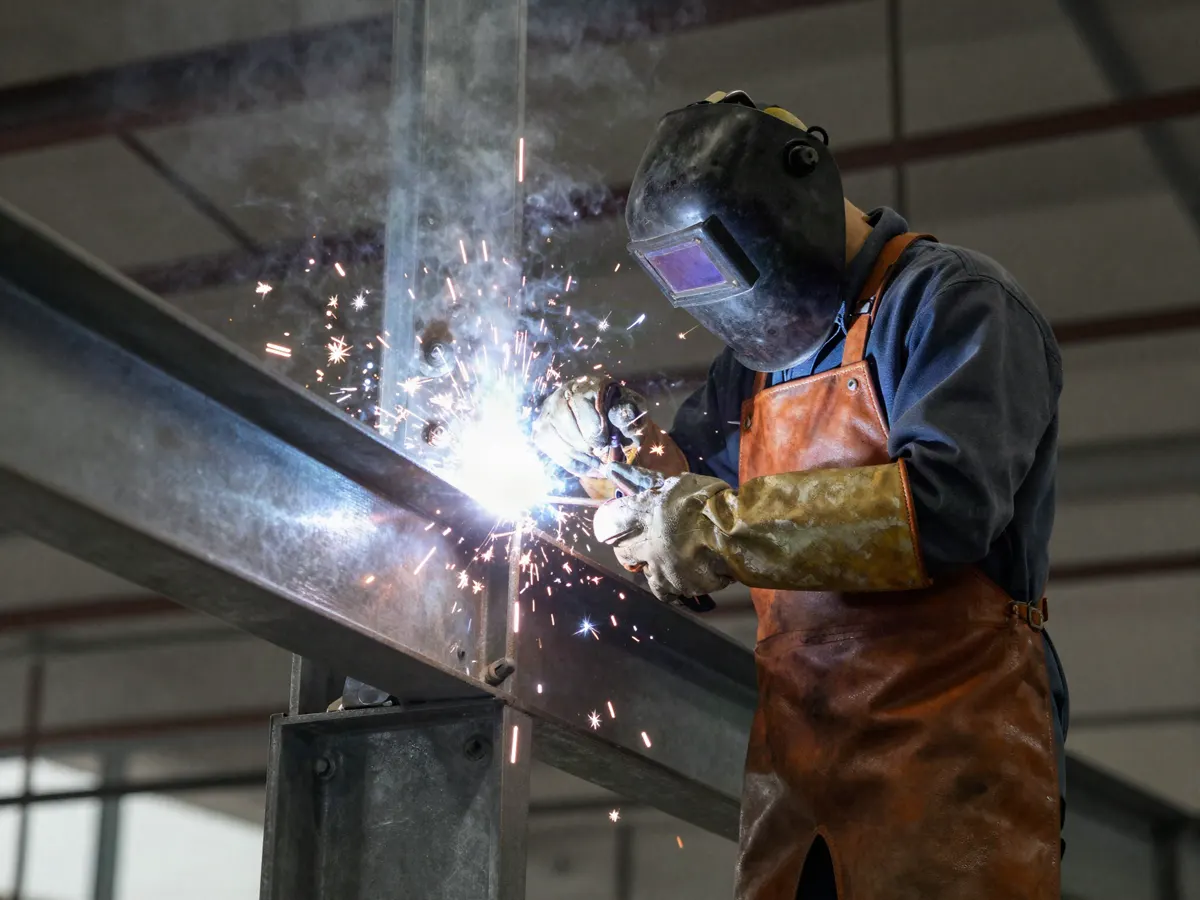 Soldador certificado reforzando una conexión estructural de acero en planta industrial